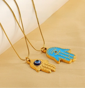 Macro detail of gold Hamsa Hand pendants with blue Evil Eye and golden snake chain