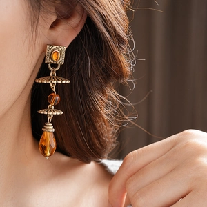 Close-up of vintage geometric earrings with amber beads and gold teardrop pendant on model