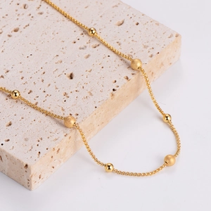 Gold stainless steel beaded necklace with alternating polished and frosted beads on travertine