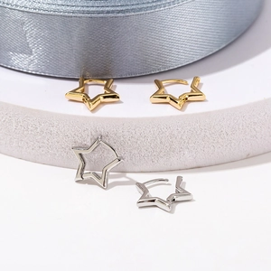 Gold and silver star-shaped huggie earrings on a white stand with silk ribbon