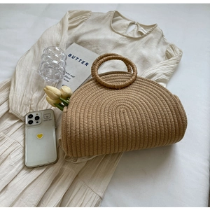 Flat lay of a semi-circular khaki woven straw tote bag on a white summer dress background