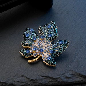 Detailed close-up of a maple leaf brooch with blue rhinestones on a black rock base
