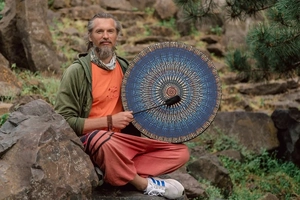 Close-up of a blue and gold mosaic shamanic drum with a wooden mallet on natural rocks