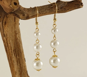Macro detail of 18k gold triple pearl drop earrings hanging on a natural branch