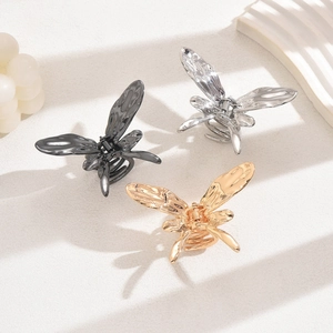 Three liquid metal butterfly hair claws in gold silver and black on a textured surface