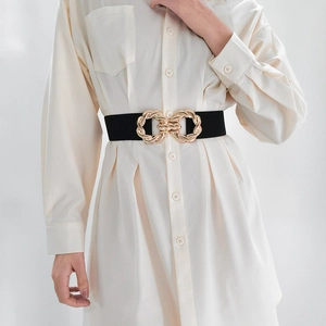 Detail of a wide black elastic waist belt featuring a twisted gold metal buckle on a model