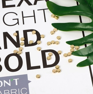 Flat lay of gold CCB flat round beads for DIY jewelry making on white card with green leaf