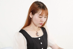 Detail view of a gold oval hollow-pattern pendant necklace worn by a female model