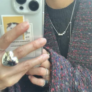 Detailed view of silver minimalist bead necklace and heart ring styled with tweed