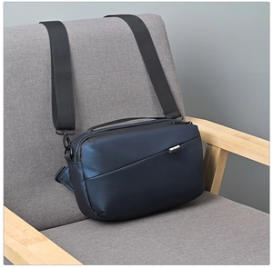 Detail of dark blue nylon crossbody bag with black zipper on a gray armchair