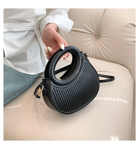 Detailed view of black pleated saddle bag with gold metal hooks and a top handle