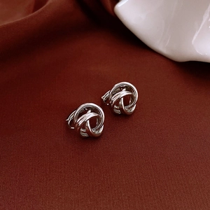 Close-up of silver knot earrings with polished finish on red satin fabric background