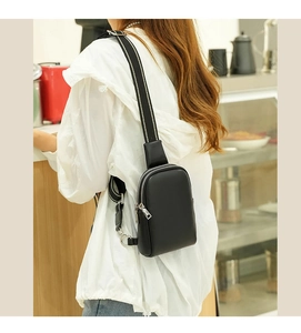 Close-up of black leather chest bag with striped wide strap worn by a model in a cafe