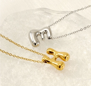 Close-up of 18K gold and silver bubble letter E and H pendants on a textured surface