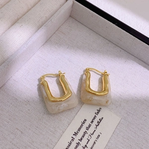 Macro shot of U-shaped gold-plated resin earrings on a textured jewelry box background