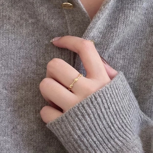 Minimalist gold heart ring worn on hand over a warm grey knitted sweater background
