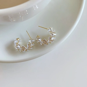Detailed view of C-shaped gold earrings with paved sparkling zircons on white ceramic
