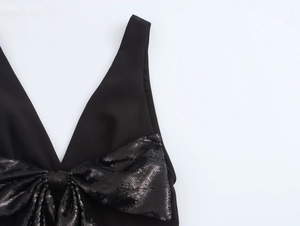 Dettaglio di un abito nero con scollo a V profondo e un grande fiocco di paillettes