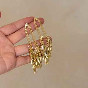 Detail of long gold tassel earrings with delicate chains and leaf-shaped metal pendants