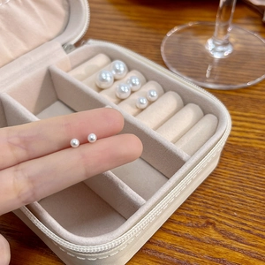 Macro shot of multiple sizes of round white pearl studs in a beige jewelry box