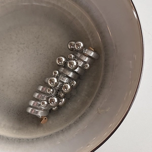 Artistic silver spiral hair tie with polished metal beads in a ceramic bowl