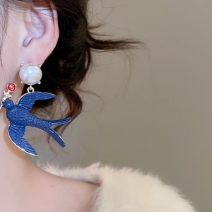 Close-up of blue swallow earring with white pearl and red flower on a model