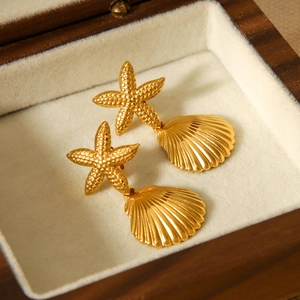 Detailed view of golden starfish and seashell pendant earrings in a wooden jewelry box