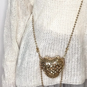 Detailed close-up of a golden hollow heart-shaped woven mini chain bag on a white sweater
