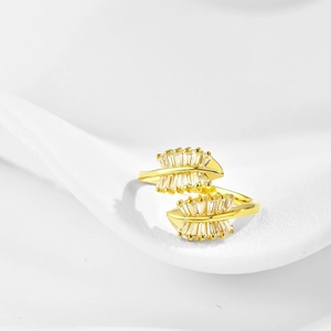 Close-up of golden leaf-shaped ring with marquise-cut clear stones on a white stand