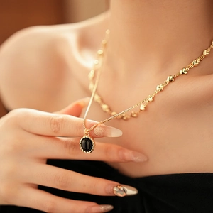 Close-up of double-layered gold heart necklace with black oval gemstone on a model