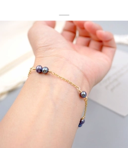 Close-up of elegant gold chain bracelet with dark purple pearls on a woman wrist