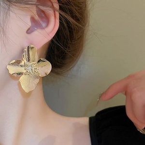 Detailed view of a gold flower earring with matte metal texture and zircons on a model
