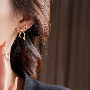 Gros plan de boucles d'oreilles nœud dorées portées sur un modèle avec détails précis