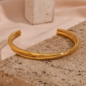 Detail of minimalist 18K gold plated double-layer open bangle on elegant satin background