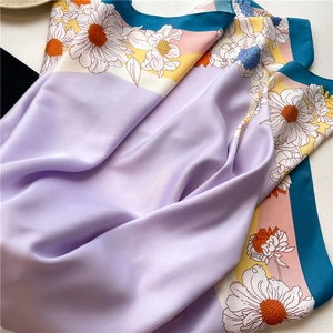 Close-up of silk square scarf with colorful daisy floral print and smooth satin texture