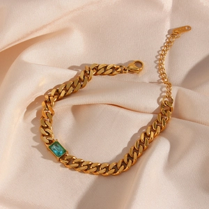 Dettaglio del bracciale a catena cubana dorata con zircone verde su sfondo in seta