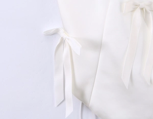 Detail of white halter top showing delicate bow ribbons and woven fabric texture
