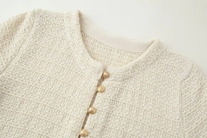 Gros plan du cardigan en maille crème avec tissu texturé et boutons dorés gaufrés