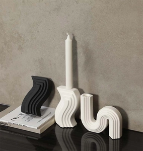 Detail of matte ceramic wavy candle holder set in black and off-white on a reflective surface