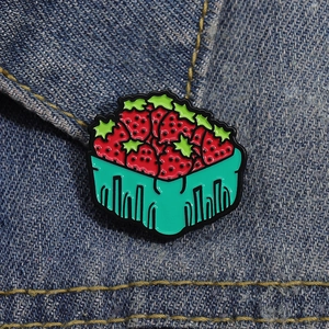 Vue détaillée d'un pin's panier de fraises en émail fixé sur un fond en denim bleu