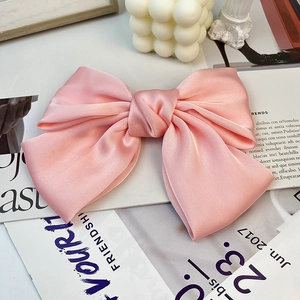 Detail of soft pink satin bow hair clip showing elegant silky texture and layered design
