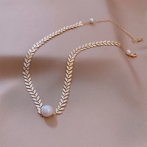 Elegant gold leaf choker necklace with central white pearl on beige silk fabric background