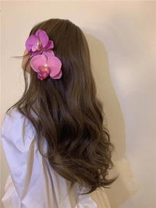 Detail of pink orchid hair clip with white pearl on brown wavy hair and white shirt