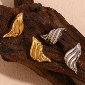 Water drop earrings with fluid texture in gold and silver finish on a wooden branch
