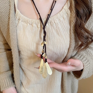 Detail of leaf-shaped gold metal pendant necklace with dark brown braided rope