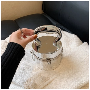 Silver cylindrical acrylic bag with curved metal handle and chain strap on fabric