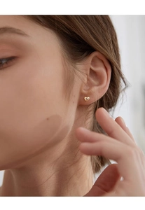 Close-up side view of a model wearing minimalist golden heart stud earrings in 925 silver