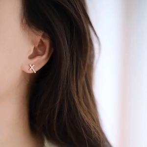 Close-up of a gold cross stud earring with micro-pave white zircons worn on a model's ear