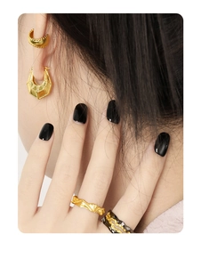 Detail of gold geometric earrings and wavy textured ring worn by a model