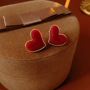 Macro shot of red flocked heart earrings with gold trim on a brown gift box stand